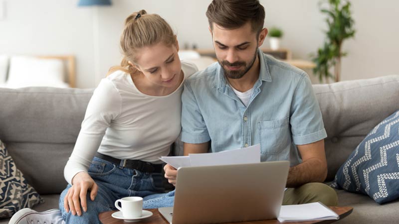 Casal sentado no sofá em frente a um portátil
